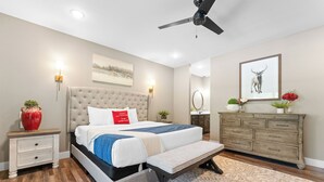 A bedroom with a bed, bedside tables, a bench, a dresser, a ceiling fan, and a painting on the wall.