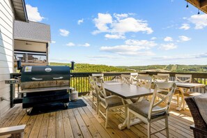 An outdoor deck with a grill, seating area, and a view of the landscape.