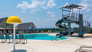 A swimming pool with lounge chairs, a yellow lamp post, and a water slide structure.