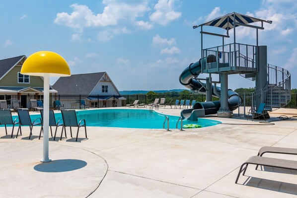 A swimming pool with lounge chairs, a yellow lamp post, and a water slide structure.