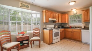 A kitchen with wooden cabinets, a stove, a sink, and a window with blinds.