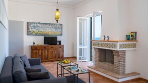 A living room with a sofa, a TV on a wooden cabinet, a fireplace, and a large window. - Villa Le Sorbe 12 in Caronia (Caronia)