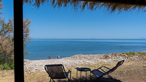 A beach view with two chairs and a table, a rocky shoreline, and a clear blue sky. - Villa Le Sorbe 12 in Caronia (Caronia)