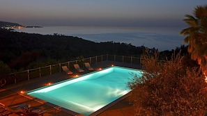 A rectangular swimming pool with a view of the sea at dusk.