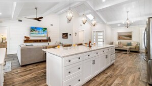 Un'ampia cucina con un'isola grande, mobili bianchi e pavimento in legno.