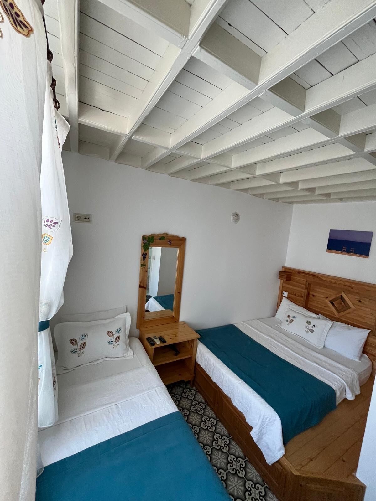 Une chambre avec deux lits, une tête de lit en bois, un miroir et un sol à motifs.