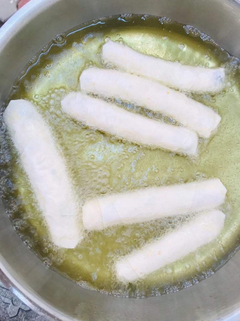 Una olla con aceite y varios objetos cilíndricos blancos friéndose.