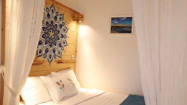 A bedroom with a wooden headboard, a bed with white bedding and decorative pillows, and a framed painting on the wall. - Adadaki Evimiz Bozcaada (Bozcaada)