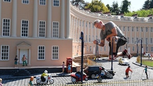 En stor byggnad med en klassisk fasad, en kullerstensgata samt små modellbilar och -figurer.