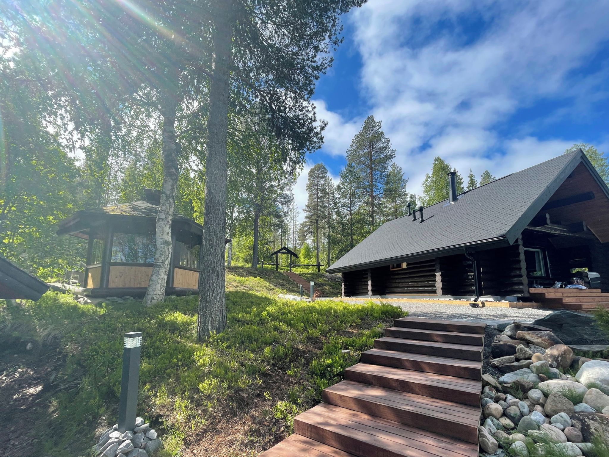 A cabin with a wooden staircase leading to a deck, surrounded by trees and a clear sky.