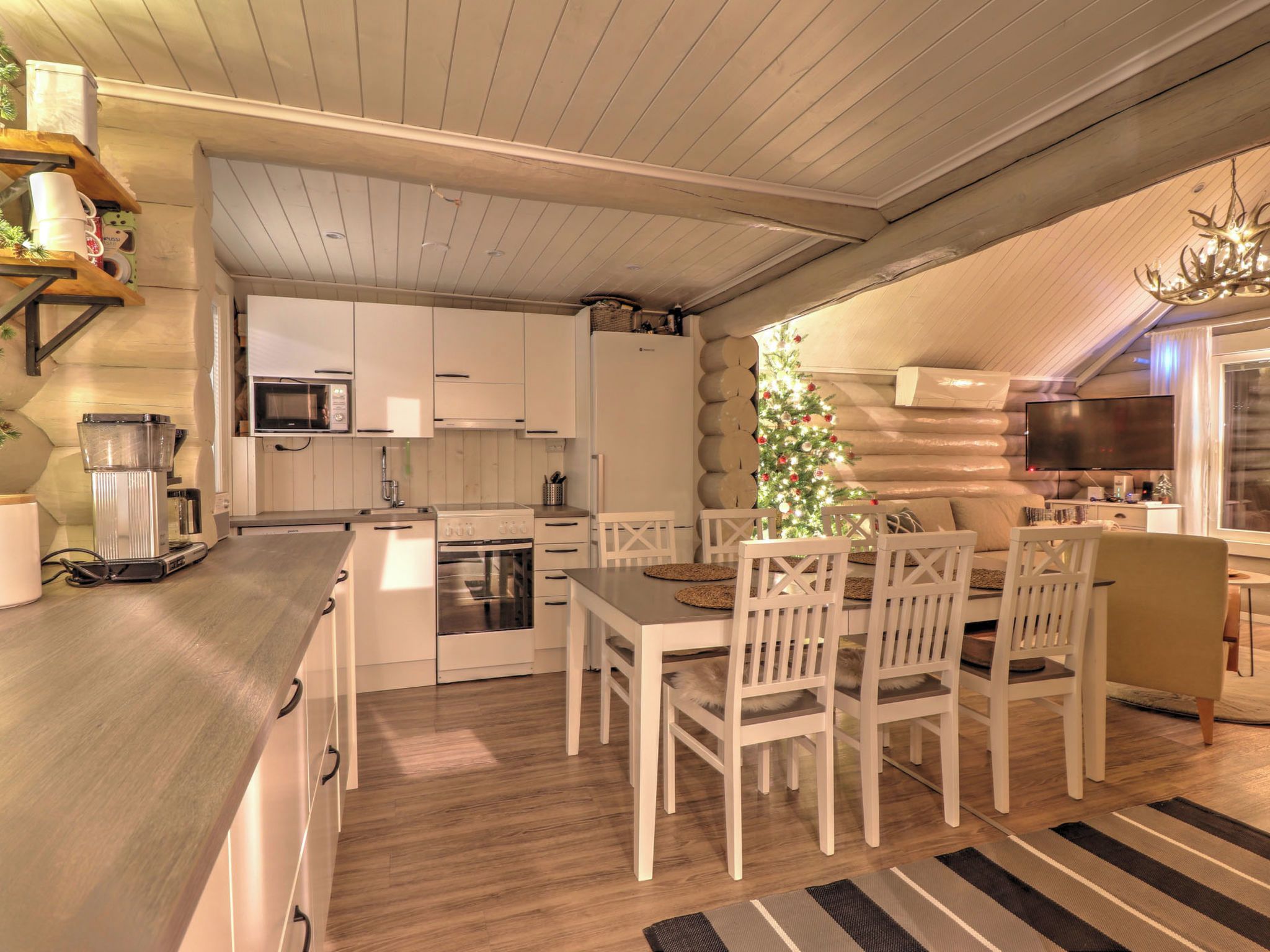 A compact kitchen with white cabinetry, a microwave, and a refrigerator. There is a dining area with a table and chairs.