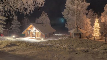 Une cabane en rondins avec un toit en pente, entourée d’arbres couverts de neige et dotée d’une terrasse en bois.