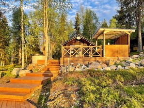 Une cabane en bois dotée d’un porche couvert et d’un escalier en pierre menant à l’entrée, entourée d’arbres et de rochers.