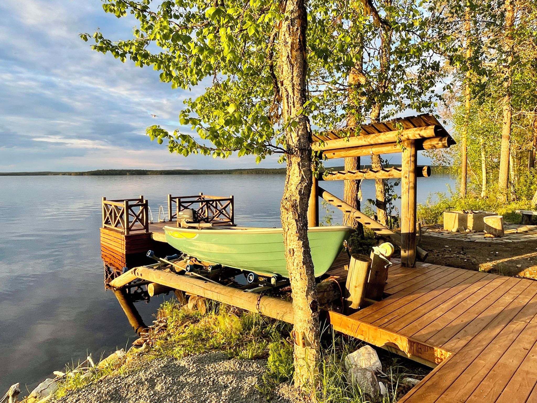 A wooden dock extending into calm water, with a boat and a covered seating area.