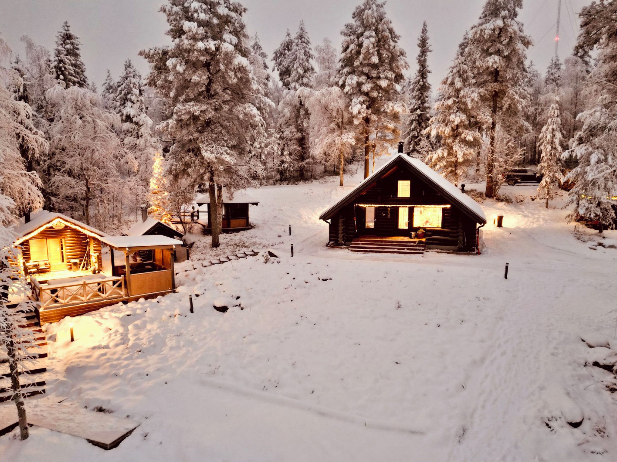 Een chalet met een houten gevel, omringd door met sneeuw bedekte bomen, en een klein houten gebouw aan de linkerkant.
