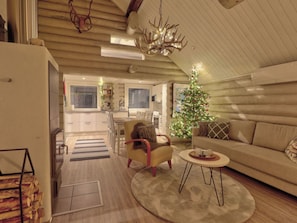 A cozy living room with a sofa, armchair, and a small round table. A Christmas tree with lights is in the corner.