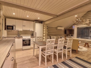 A modern kitchen with white cabinetry, a dining area with wooden chairs, and a large window with blinds.