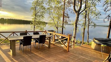Une terrasse en bois avec une table et des chaises donnant sur un lac paisible.