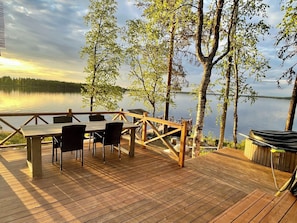 A wooden deck with a table and chairs overlooking a calm lake.