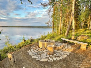 A lakeside campsite with a fire pit and a bench.