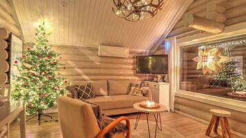 A cozy log cabin interior with a Christmas tree, a chandelier, and a television.