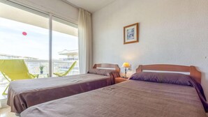 Una camera d'albergo con due letti, una finestra con tende, un tavolino con una lampada e una sedia.