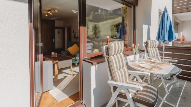 Un espace extérieur moderne, aménagé avec des sièges, une cloison en verre, des chaises à rayures et une table dressée pour le repas.