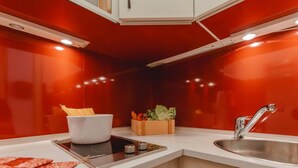 Une cuisine compacte avec un crédence rouge, un plan de travail blanc, une cuisinière encastrée et un évier.