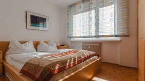 Une chambre à coucher avec un lit, une table de chevet, une fenêtre avec des stores et un radiateur.