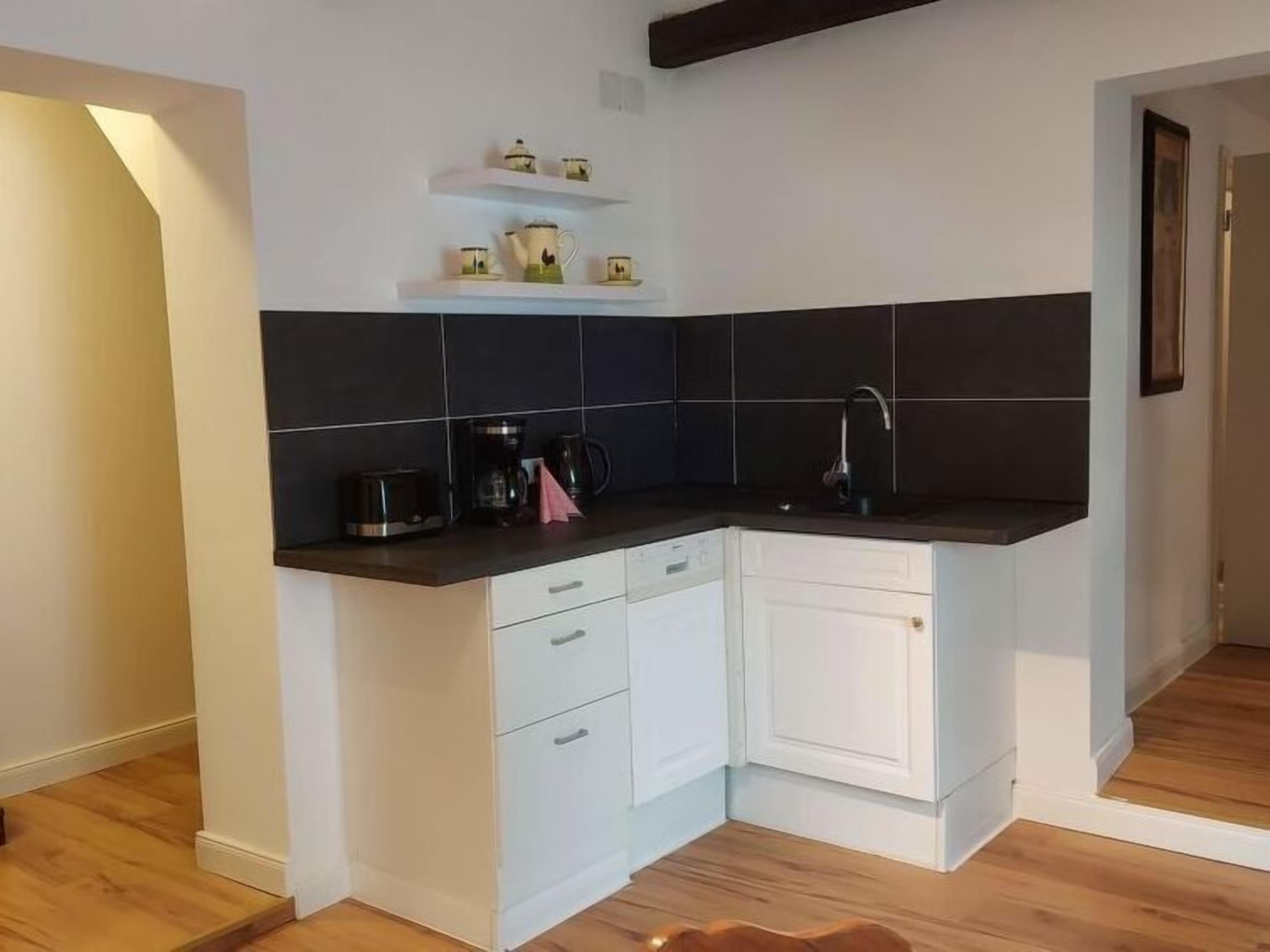 A compact kitchen with white cabinetry, a black countertop, and a small shelf above the sink.