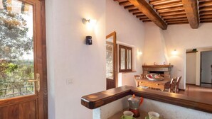 A cozy kitchen with a wooden ceiling, a dining area with a table and chairs, and a view of trees through a window. - Fonte al Tesoro by Interhome (Sassofortino)