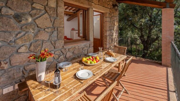 An outdoor wooden deck with a stone wall, a dining table set with plates, glasses, and a fruit bowl, and a potted plant. - Fonte al Tesoro by Interhome (Sassofortino)
