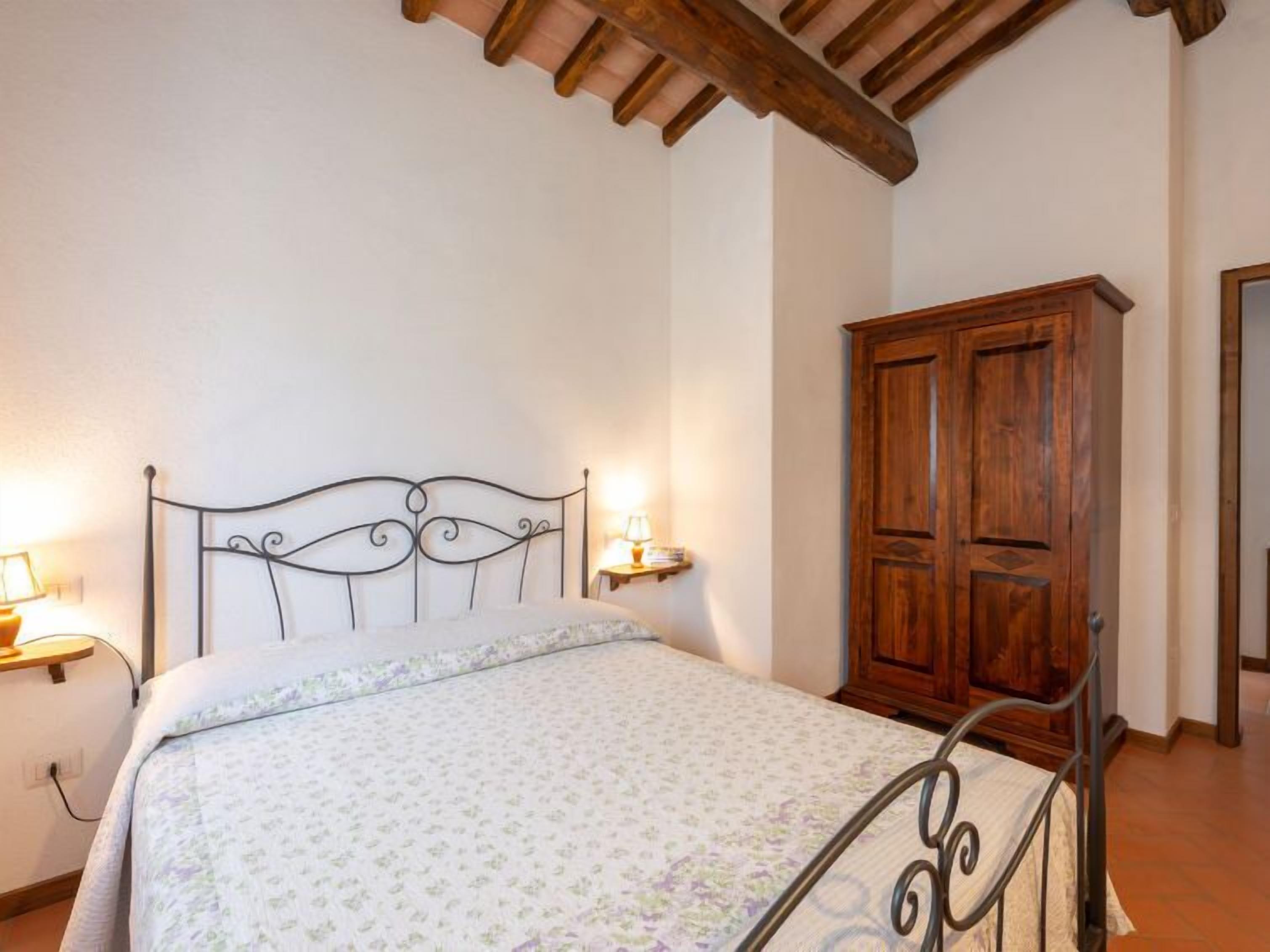 A bedroom with a metal bed frame, a wooden wardrobe, and two bedside lamps.