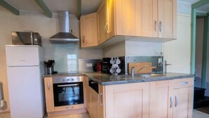 A compact kitchen with a built-in oven, a microwave, and a stove. There are wooden cabinets and a tiled floor. - Vacation home Ty Coz by Interhome (Pleurtuit)