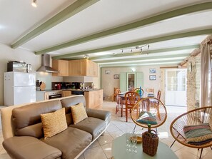 A modern kitchen with wooden cabinets, a dining area with a table and chairs, and a living room with a sofa and a coffee table. - Vacation home Ty Coz by Interhome (Pleurtuit)