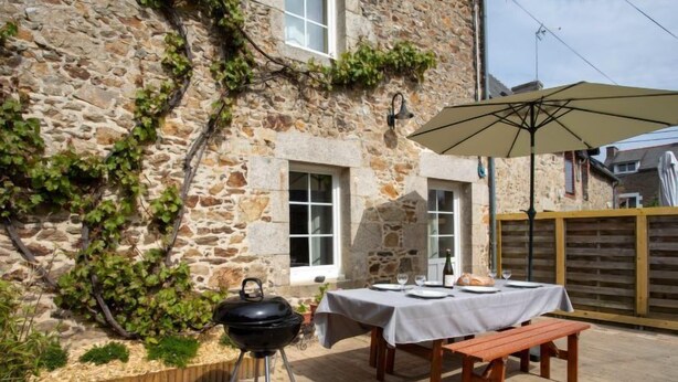 A stone building with a barbecue grill and a table set for dining, surrounded by a wooden fence and a wooden bench. - Vacation home Ty Coz by Interhome (Pleurtuit)