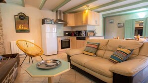 A cozy living room with a sofa, a small table, a chair, and a kitchen area with wooden cabinets and a stove. - Vacation home Ty Coz by Interhome (Pleurtuit)