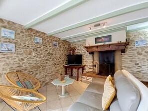 A cozy living room with a stone wall, a fireplace, a television, and comfortable seating.