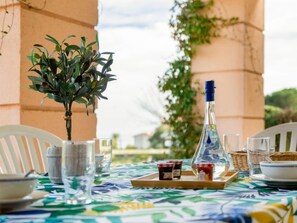 A table set with a bottle, glasses, and jars of jam, with a potted plant and a view of greenery in the background. - Le Belvédère (V2 009) by Interhome (Agay Village Cap Esterel)