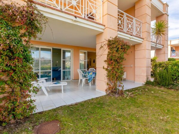 A residential building with a balcony, a covered patio area, and a grassy garden. - Le Belvédère (V2 009) by Interhome (Agay Village Cap Esterel)