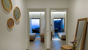 A hallway leading to a bedroom with a view of the sea. There are two beds, a chair, and a small table with a vase. - Villa Erato in Triantaros Tinos (Tinos island)
