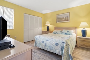 A bedroom with a bed, bedside tables, a desk with a computer, a wardrobe, and a painting on the wall.