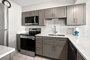 A modern kitchen with stainless steel appliances, grey cabinetry, and a white countertop. - Oceanfront condo overlooking sweeping sands & awesome views w/beachfront pool, expansive balcony (North Myrtle Beach)
