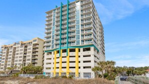 A multi-story hotel with balconies, a parking garage, and a beach view. - Seaside Resort- modern beach destination! (North Myrtle Beach)