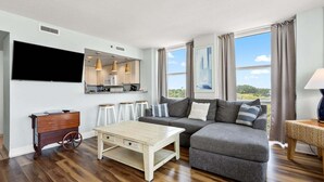 A modern living room with a sofa, a coffee table, a TV, and a kitchen area with a microwave. - Seaside Resort- modern beach destination! (North Myrtle Beach)