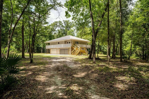 Uma casa de dois andares com varanda e garagem, cercada por uma floresta.