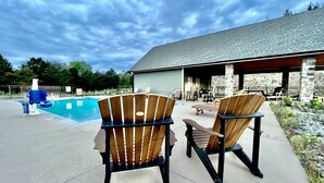 Two Adirondack chairs facing a pool and a covered patio area with outdoor furniture. - New! Private 5BR 5,000 SqFt Lake House on 7 Acres (Dandridge)