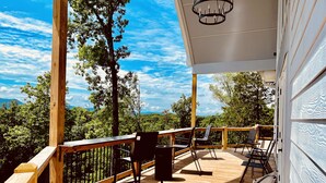 A wooden deck with outdoor seating and a view of a forested landscape. - New! Private 5BR 5,000 SqFt Lake House on 7 Acres (Dandridge)