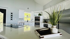 A modern kitchen with white cabinetry, a central island, and a large window. - New! Private 5BR 5,000 SqFt Lake House on 7 Acres (Dandridge)