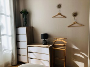 Un dormitorio con un aparador de madera, una mesita de noche con lámpara y dos perchas de madera fijadas a la pared.